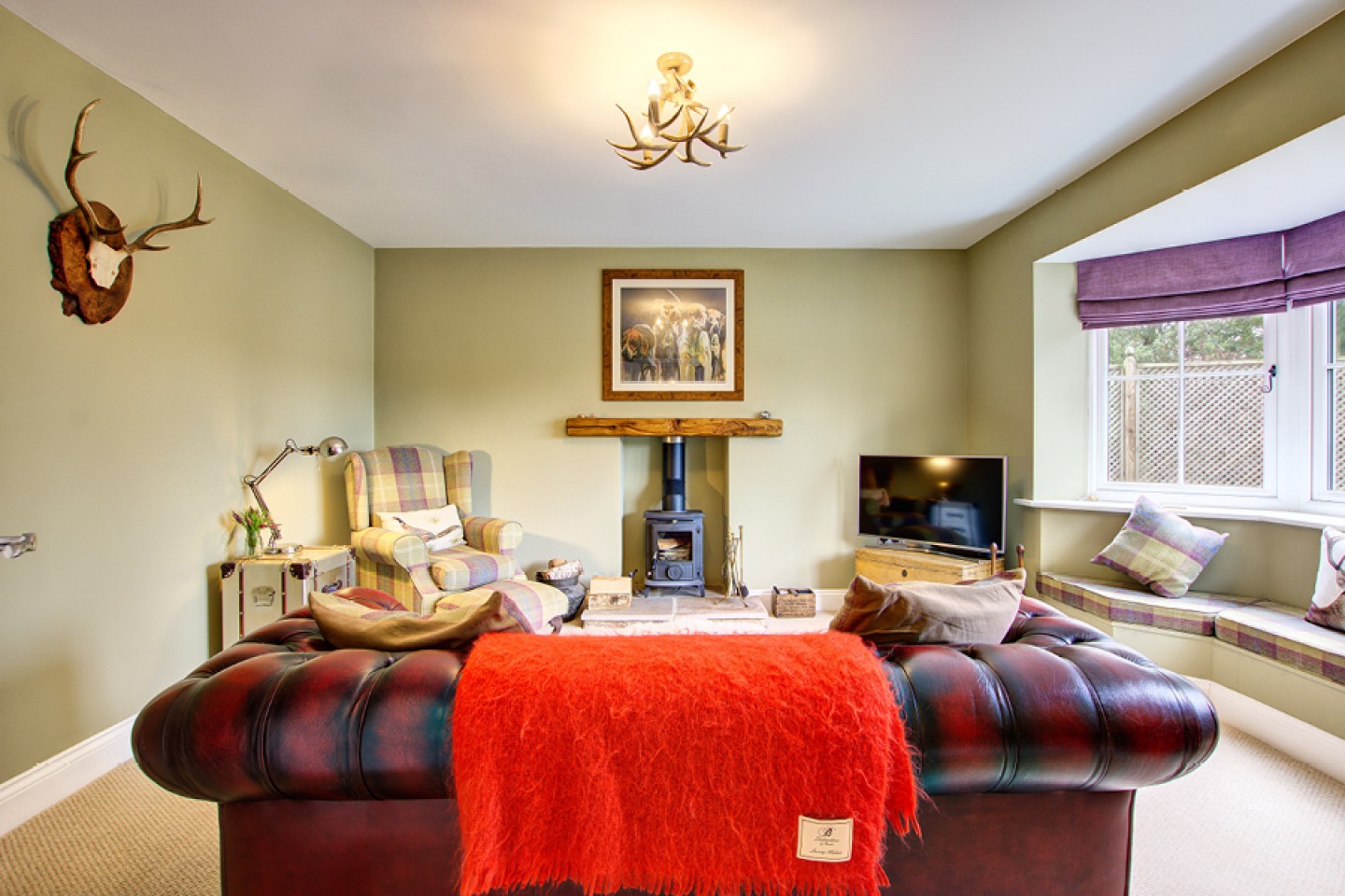 Cosy lounge with woodturning stove, leather Chesterfield and tartan armchair